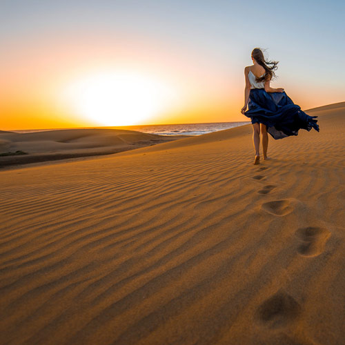 En kvinne som går i en ørken ved havet i solnedgang